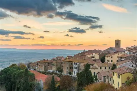Cortona at sunset — the Tuscan hilltop city with its terracotta rooftops and medieval towers glowing in the golden evening light