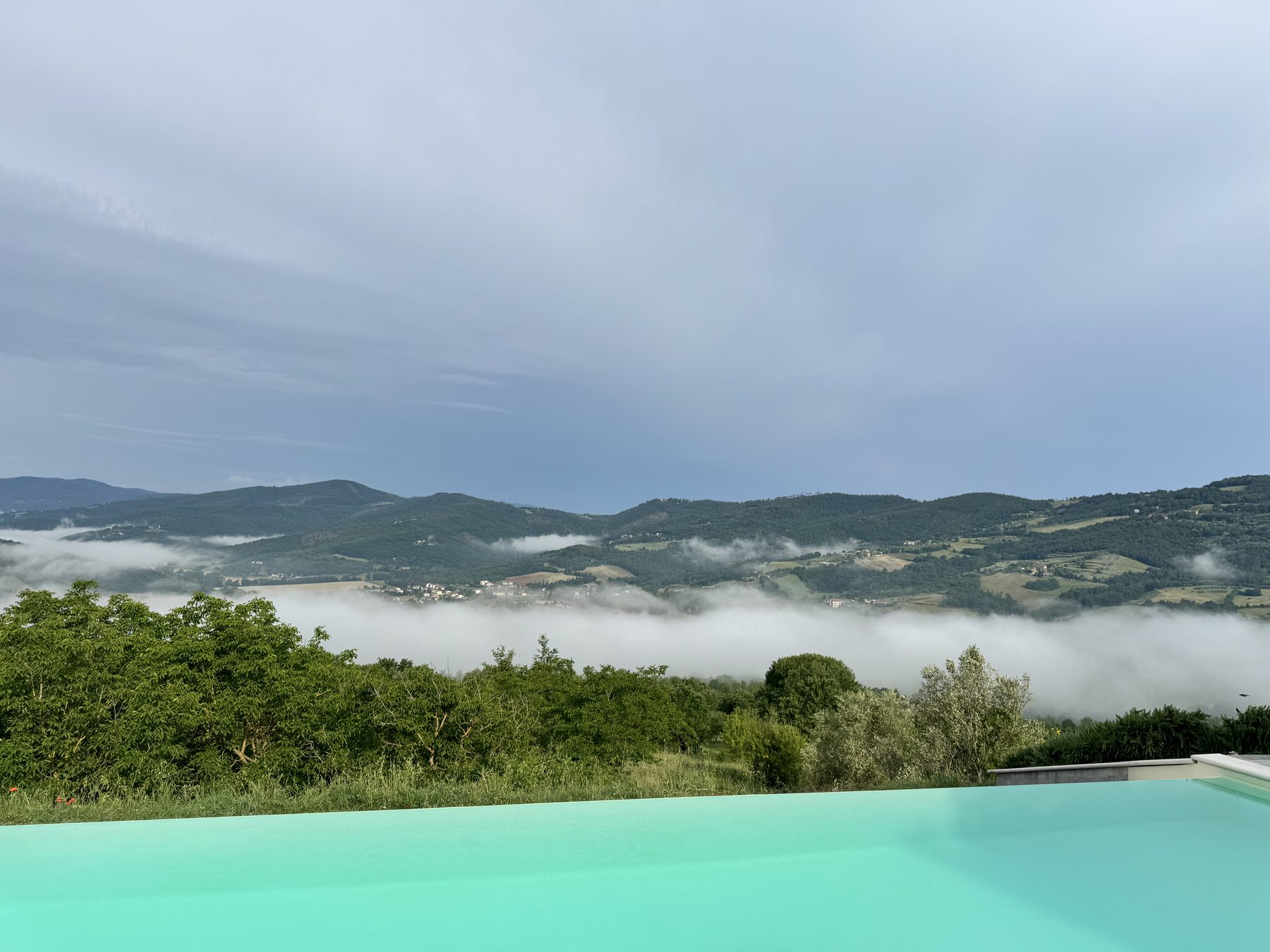Casa Luna infinity pool edge at dawn with morning clouds drifting through the Umbrian hills, Niccone Valley